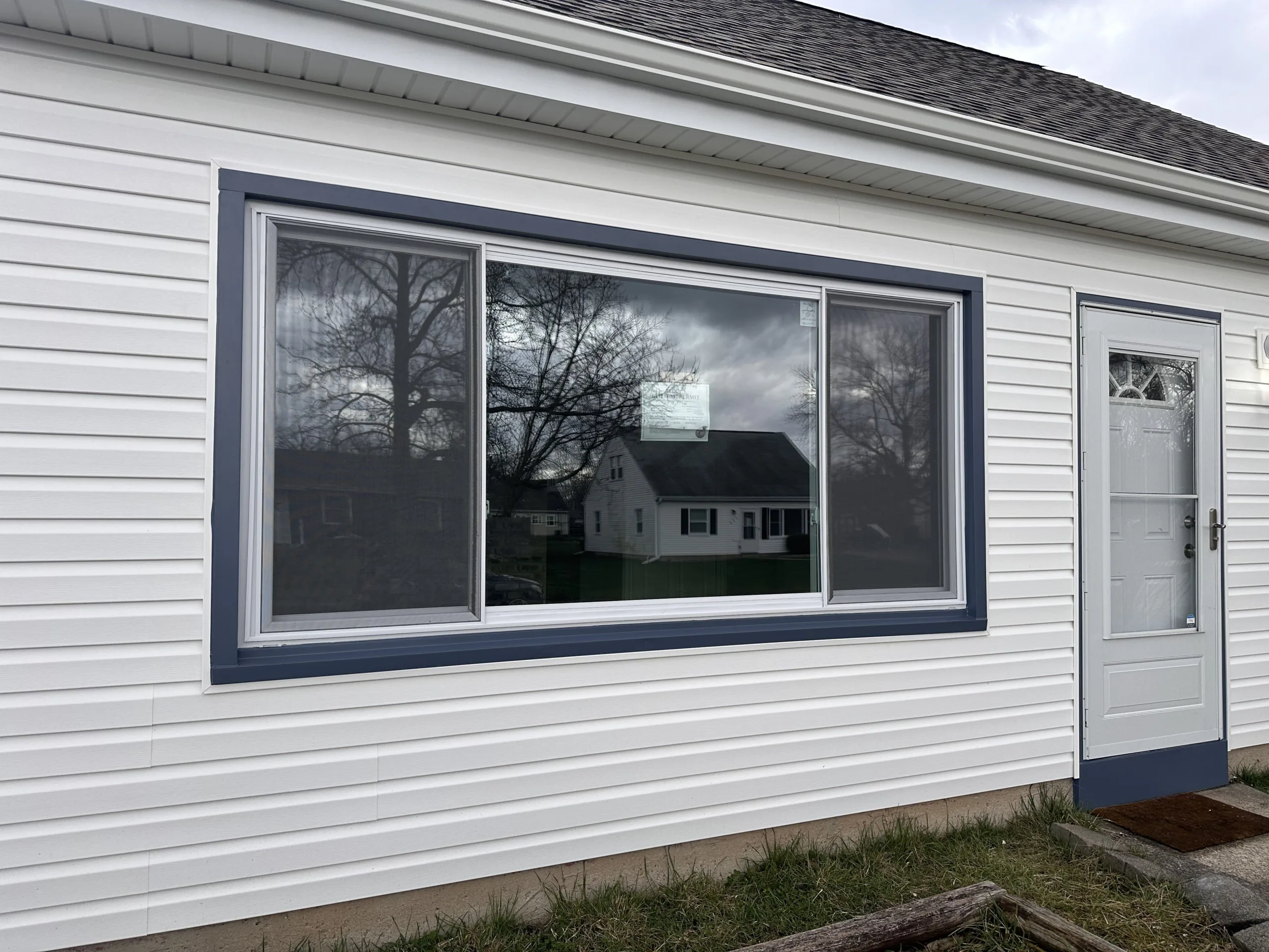 IMG_9779 Residential facade with a large window reflecting the opposite house and a light blue entrance door.